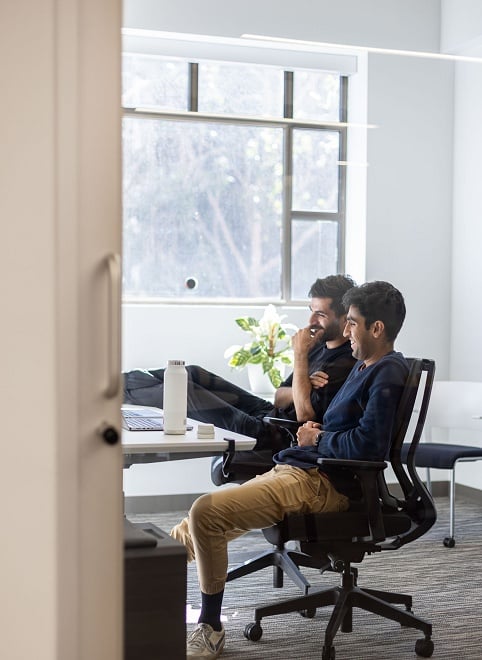 Two coworkers sitting in office space looking at a monitor Two coworkers sitting in office space looking at a monitor