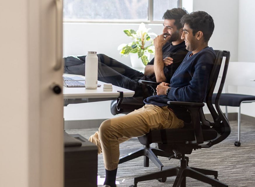 Two male coworkers sitting in office space looking at a monitor Two male coworkers sitting in office space looking at a monitor