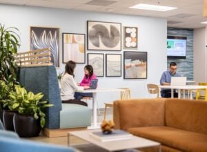 Two women and one man sitting at tables and work booths in reception area