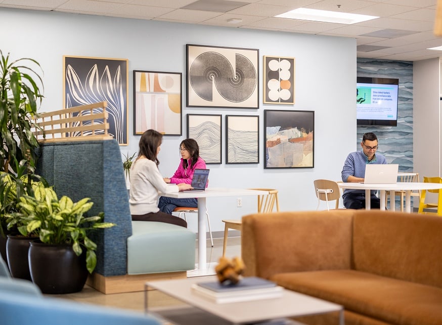 Two women and one man sitting at tables and work booths in reception area Two women and one man sitting at tables and work booths in reception area