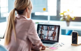 Back view of female on video call with colleagues on online meeting with laptop at home.